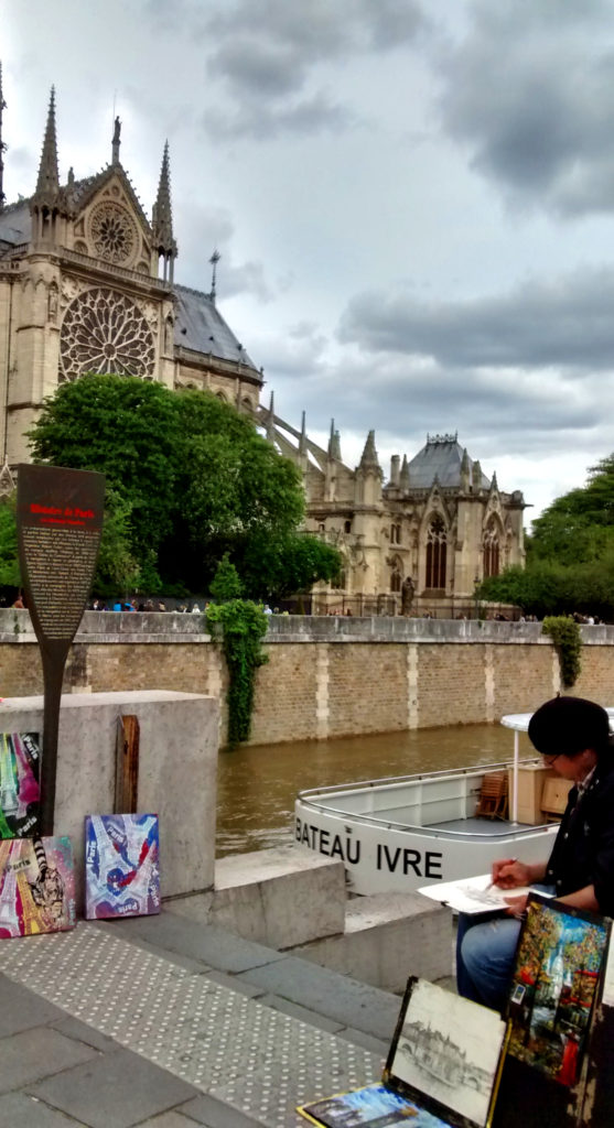 Artista desenhando à beira do Rio Sena, na margem oposta à Catedral de Notre Dame